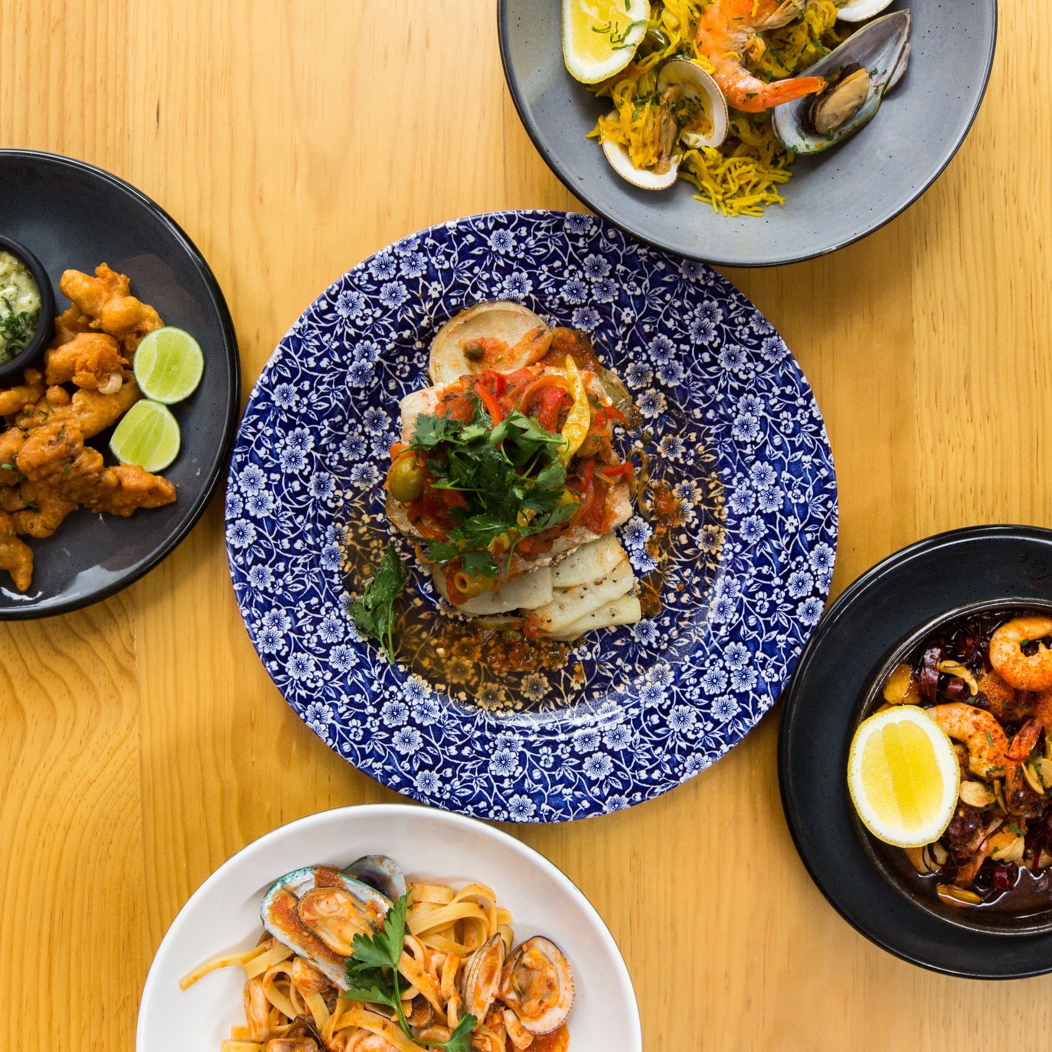 Vista aérea de platos de mariscos, pasta y paella sobre mesa de madera