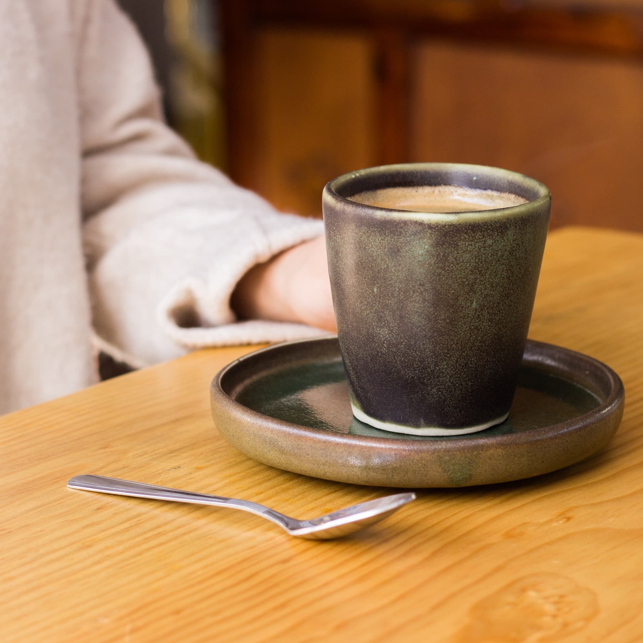 Taza artesanal de espresso sobre plato de cerámica y mesa de madera